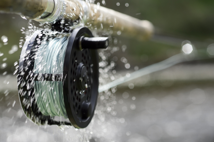 A fly fishing reel sends water flying as it spins at high speed while letting the line out fast. class=