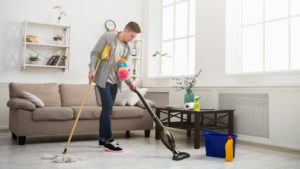 Young man cleaning house with lots of tools. Tired guy washing floor with mop and vacuum cleaner, copy space