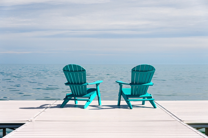 two blue wooden deck chairs facing the lake